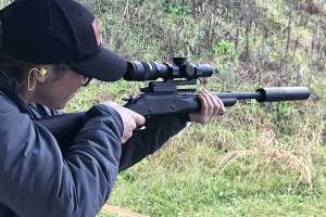 Woman target shooting rifle suppressor optics hearing protection